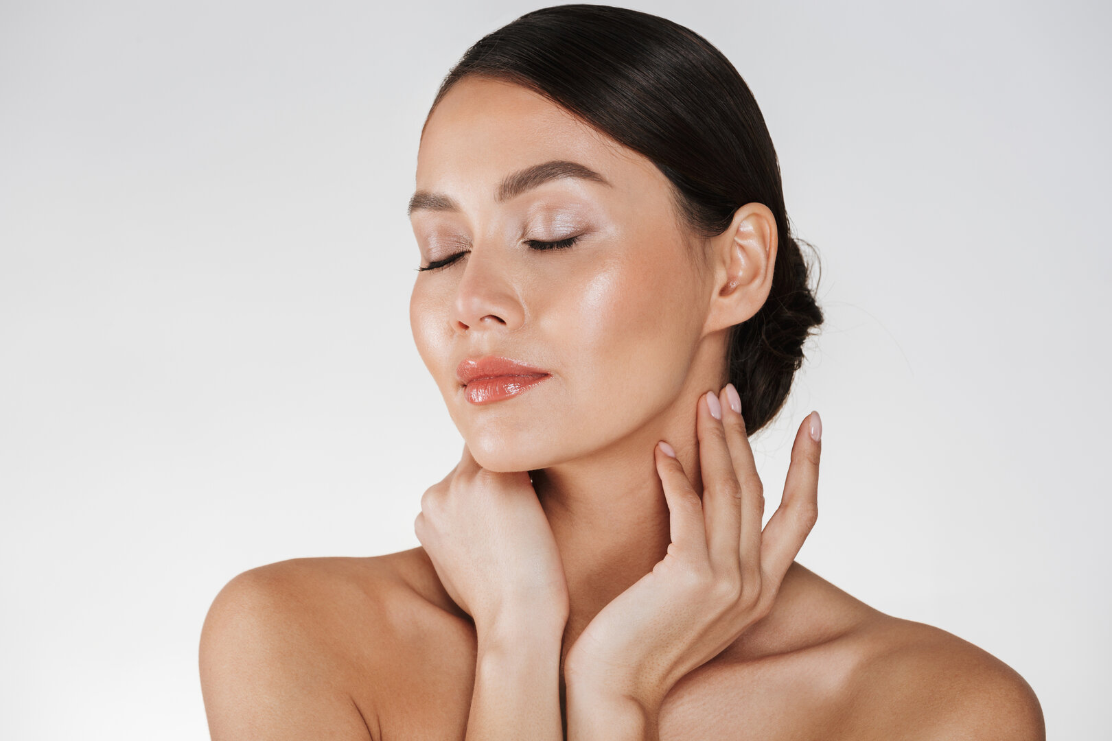 Mujer con ojos cerrados tocando suavemente su rostro y cuello en una imagen de estética facial