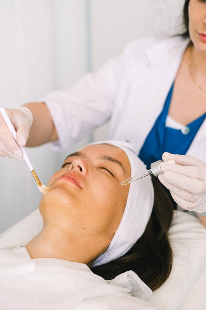 Paciente recibiendo la aplicación de un tratamiento facial con brocha y gotero en clínica estética