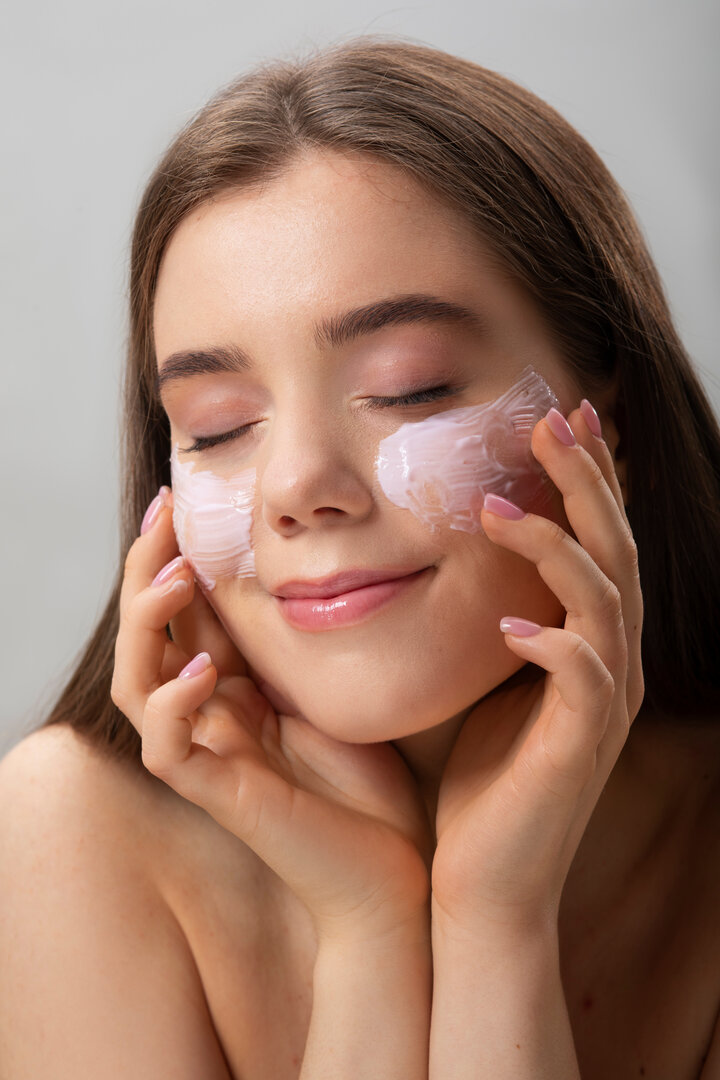 Mujer aplicando crema facial en las mejillas con expresión relajada