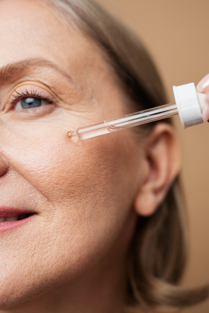 Primer plano de piel facial madura con sérum aplicado mediante gotero