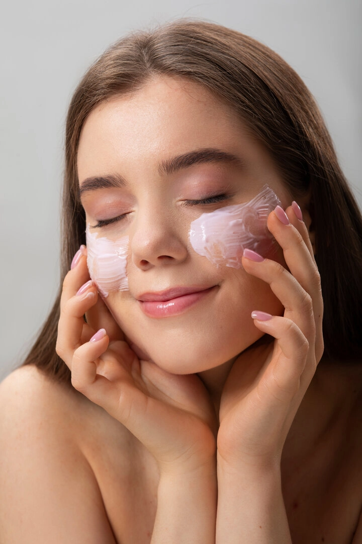 Mujer aplicando crema facial en las mejillas con expresión relajada